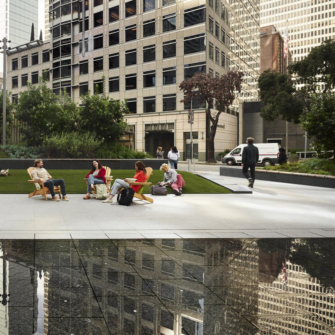 People sitting by water feature on plaza enjoying live music
